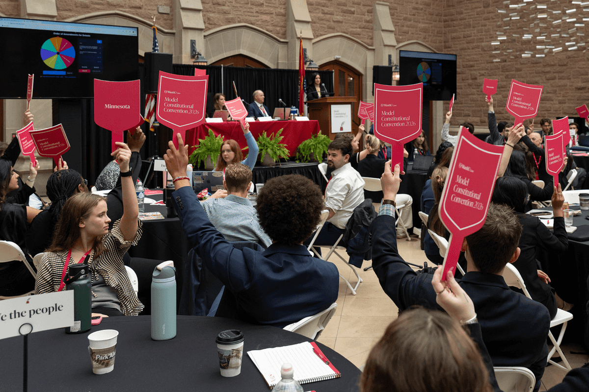 Students sitting down around tables at an event, each holding up a sign.