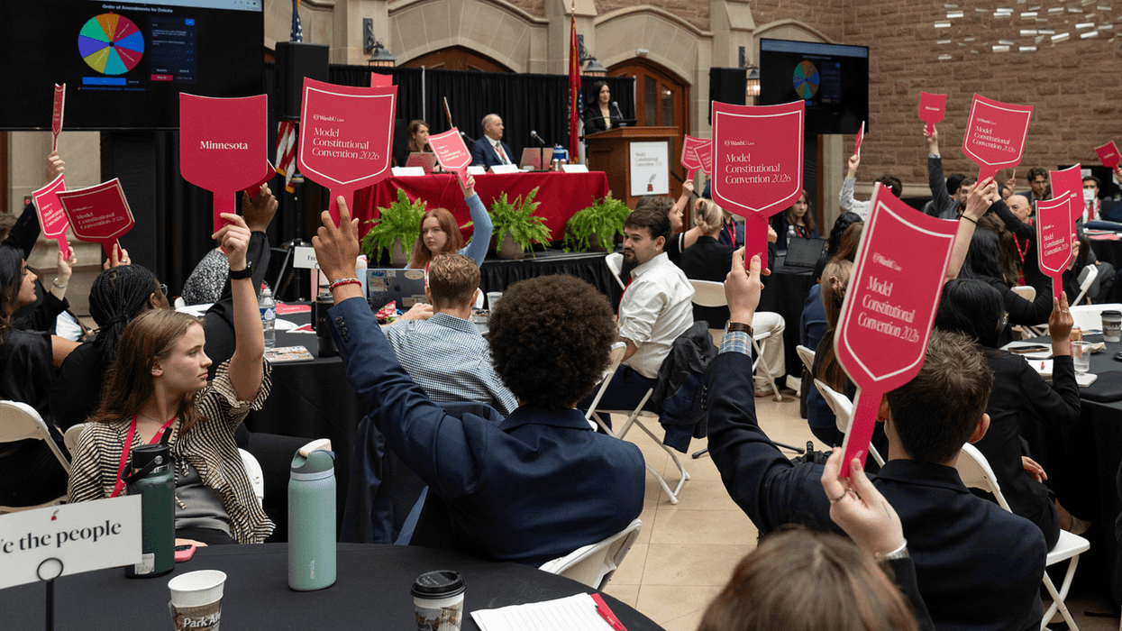 Students sitting down around tables at an event, each holding up a sign.