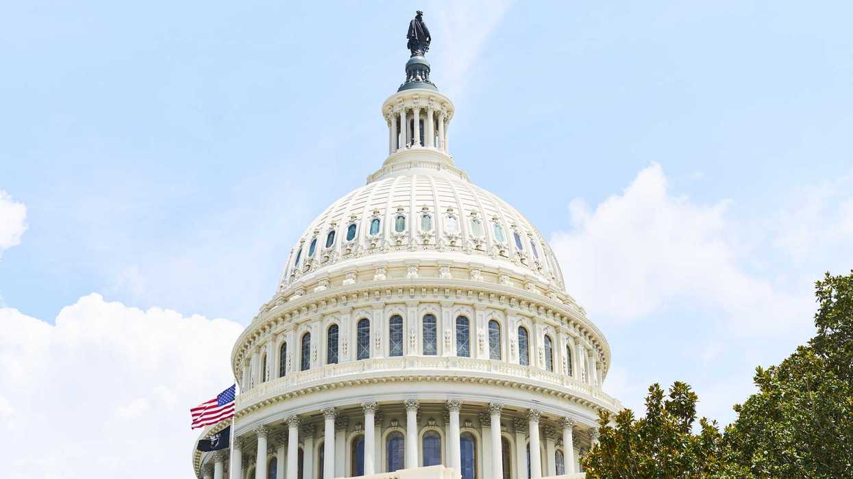 The dome of the United States Capitol Building in Washington, D.C., stands tall against a blue sky with the American flag waving proudly