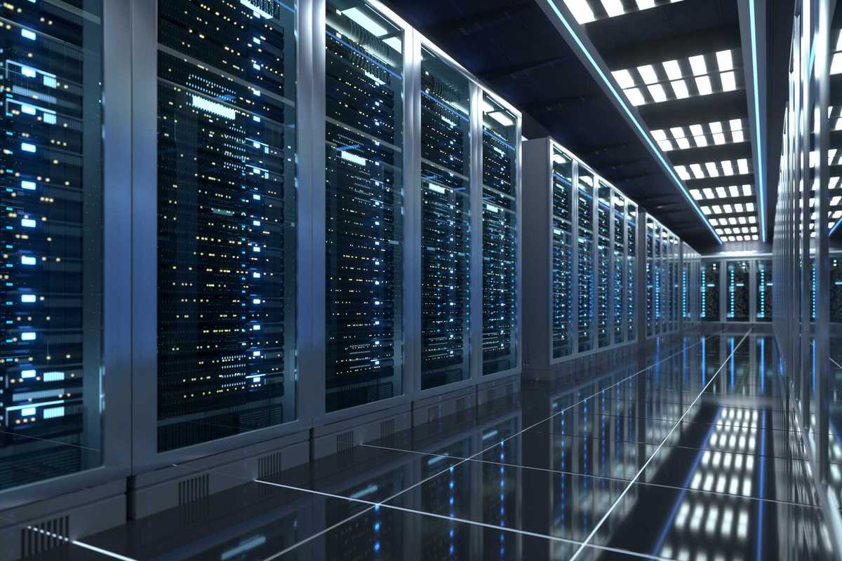 This wide angle shot shows a fully operational modern data center hallway, lined with rows of fully operational server racks behind glass panels. The highly polished reflective floor mirrors the glowing indicator lights and overhead ceiling lights, creating a sleek, futuristic industrial tech environment focused on enterprise cloud computing and digital data storage.