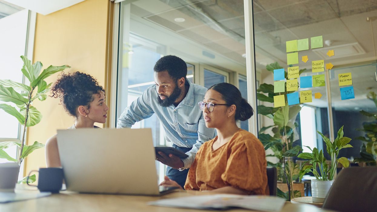 Three diverse professionals  in business attire smiling and posing in an office