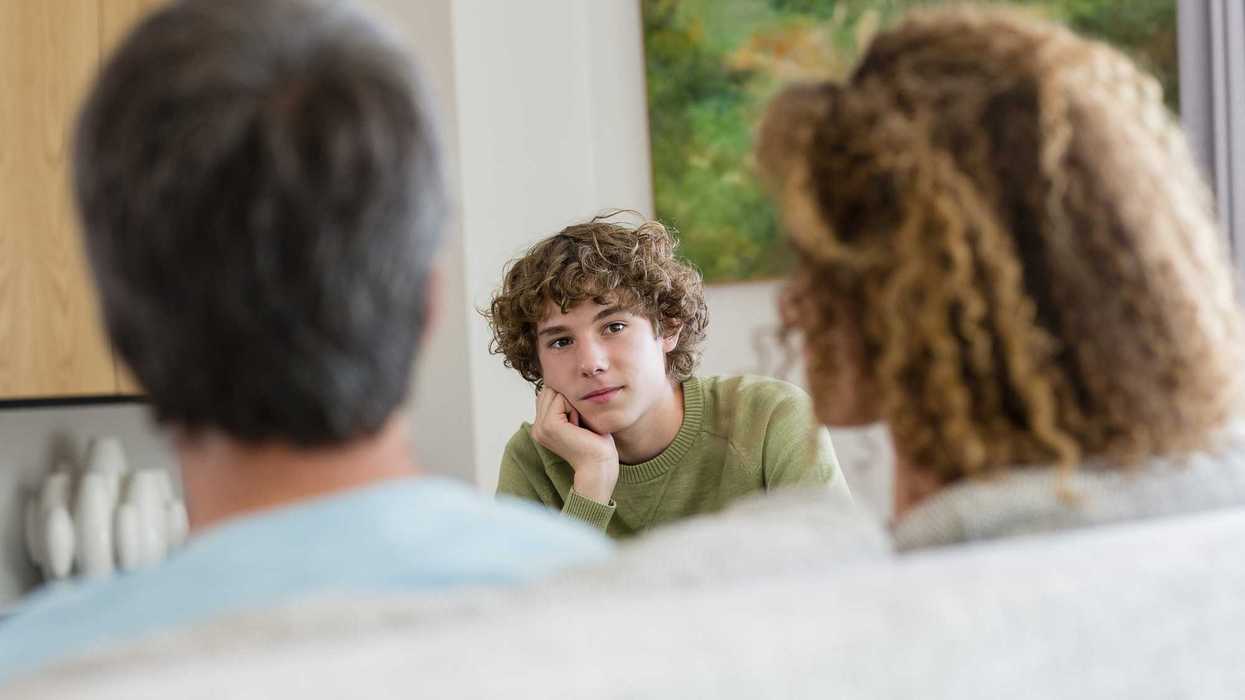 Two parents sitting down on a couch across from their teen son, looking at each other.