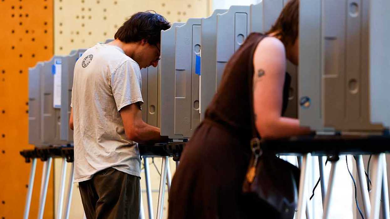 Two people at separate voting booths, filling out a ballot.