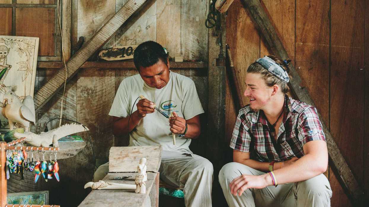 Two people sitting next to each other as one person works with clay.