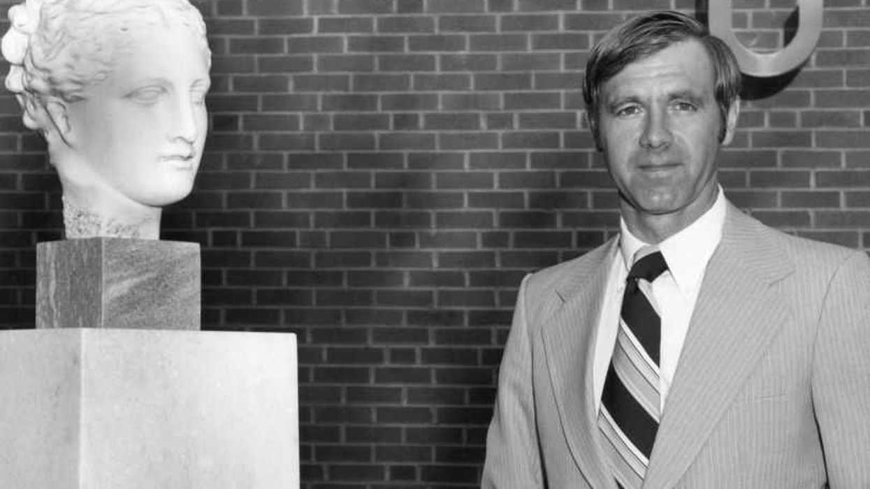 William H Foege standing next to a bust of Hygeia.