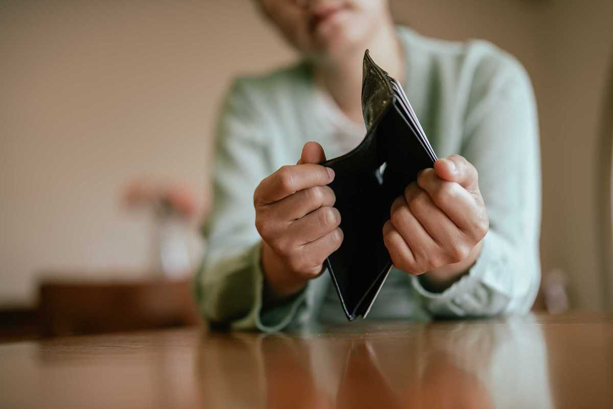 Woman holding out an empty wallet at a table.