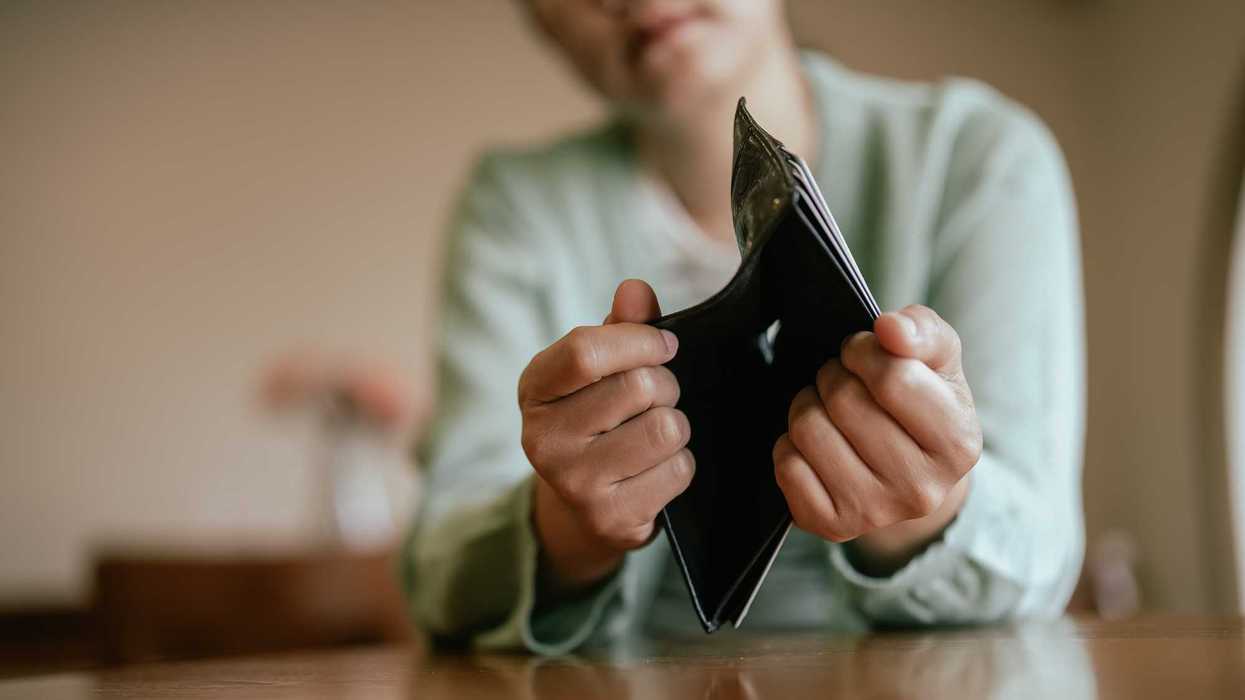 Woman holding out an empty wallet at a table.