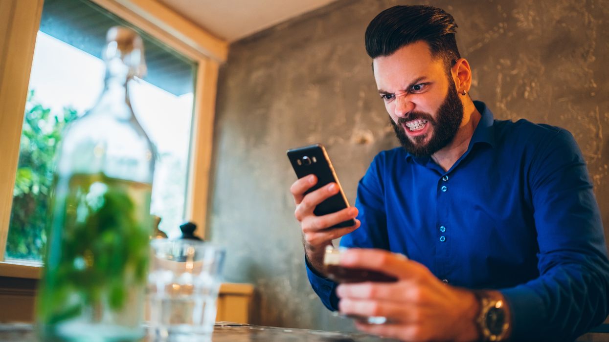 Young man looking angry at display of his smartphone.